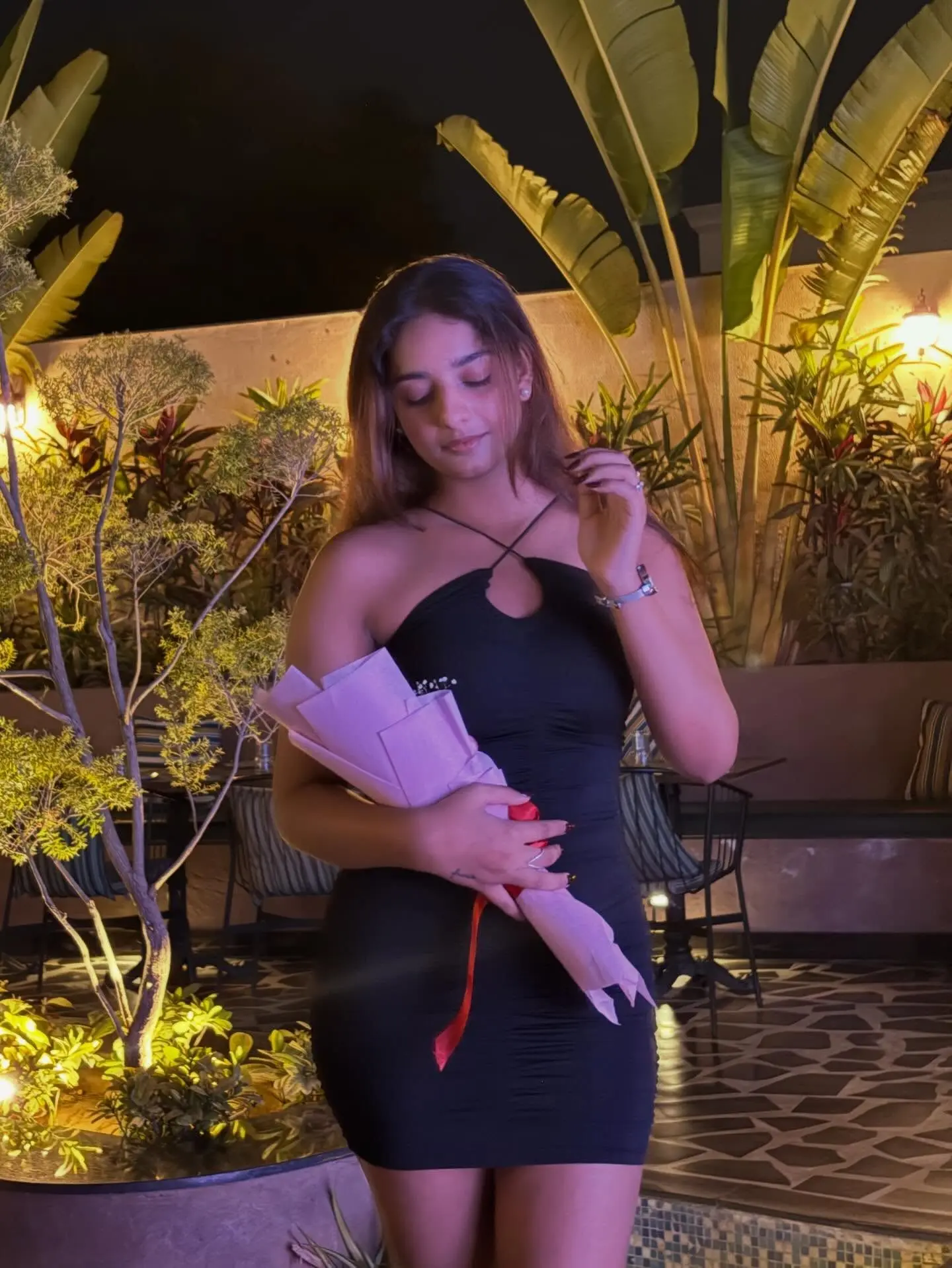 Vanshika Tanwani in a black halter cut-out mini dress holding a bouquet at night