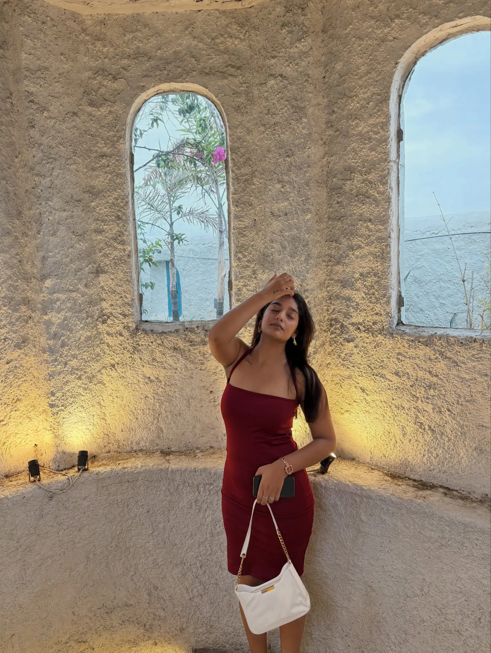 Vanshika Tanwani in a wine-red strappy bodycon dress against a lit stone wall